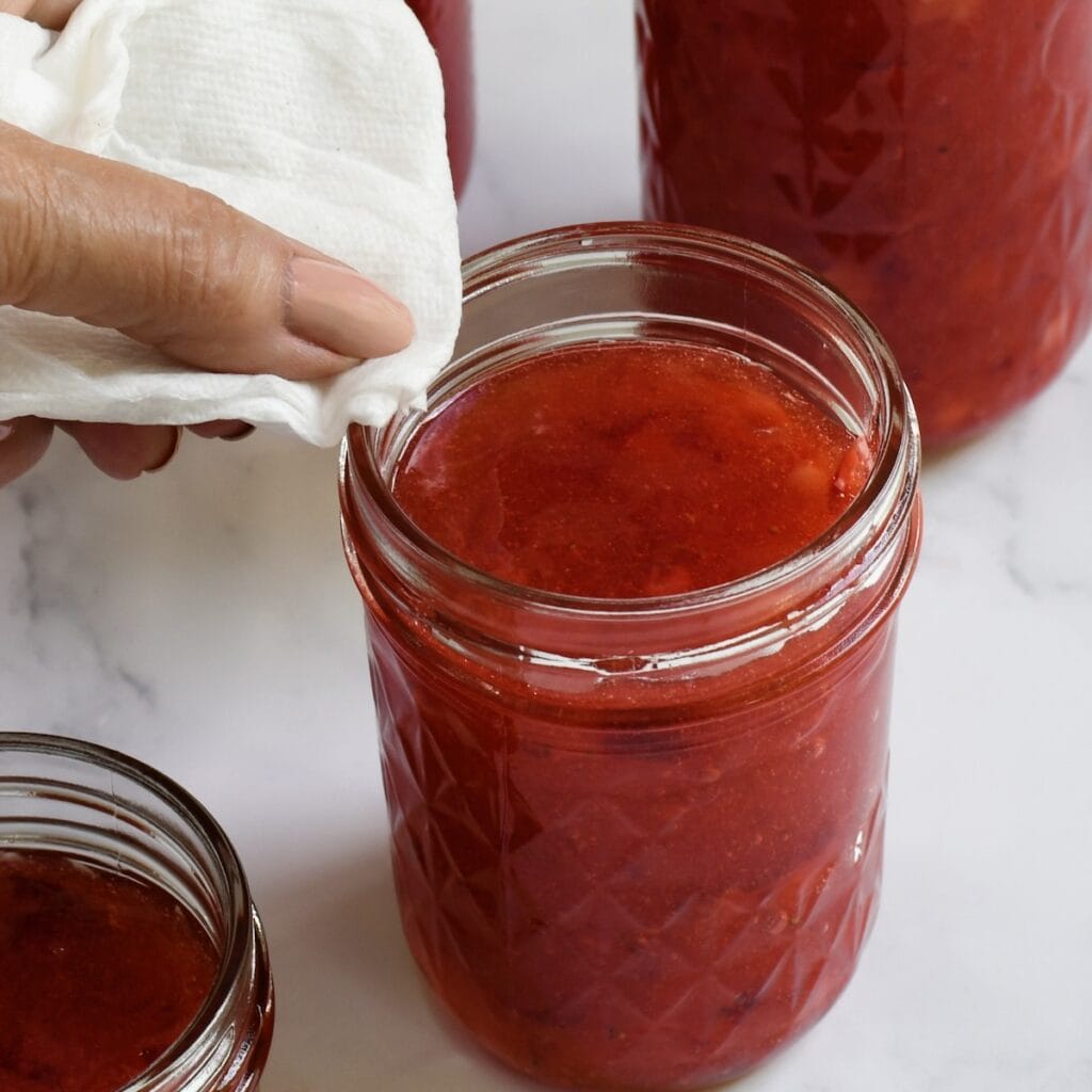 Hand wiping the edge of the jar of strawberry rhubarb freezer jam.
