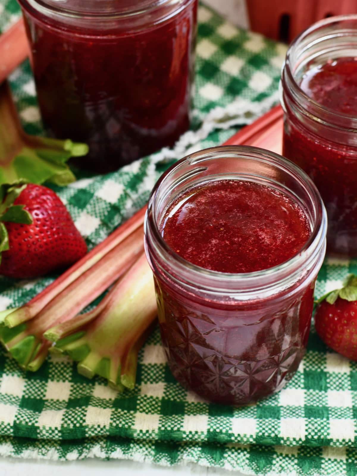 Jar of strawberry rhubarb jam with jello on a green and white linen.
