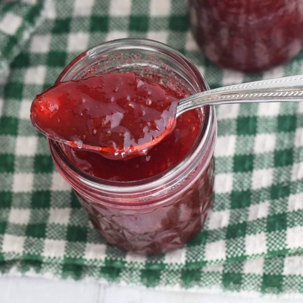 Strawberry rhubarb jam with jello in a jar with a spoon scooping some up.