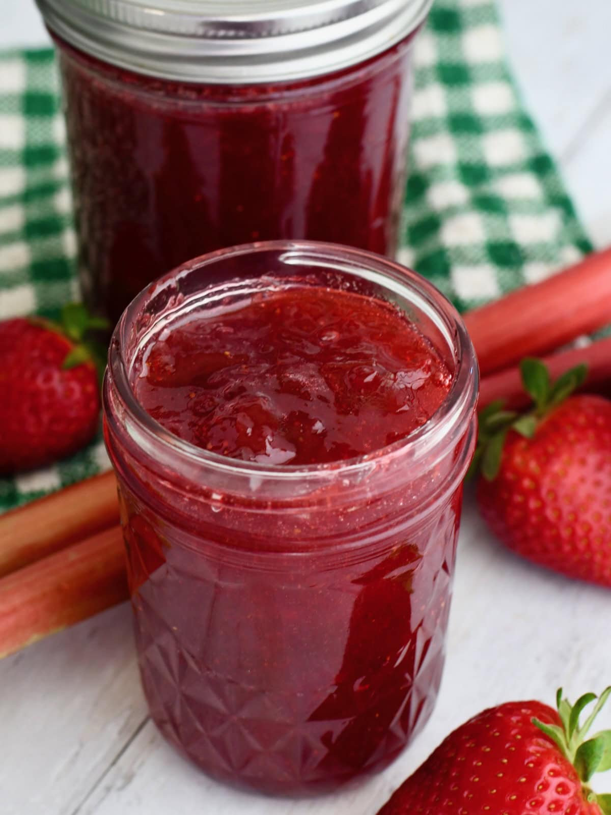 Small jar of strawberry rhubarb jam with jello next to fresh strawberries and rhubarb.