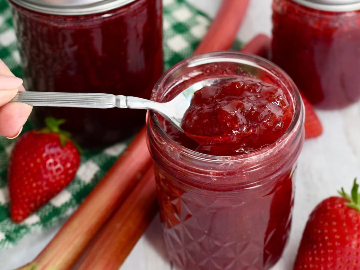 Hand scooping up a spoonful of strawberry rhubarb jam with jello.
