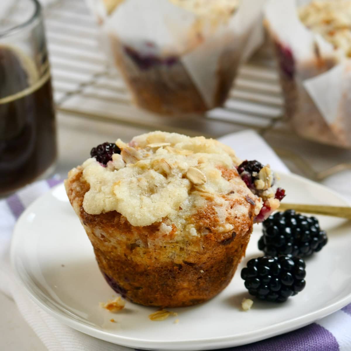 Banana blackberry muffin on a plate next to some fresh blackberries.