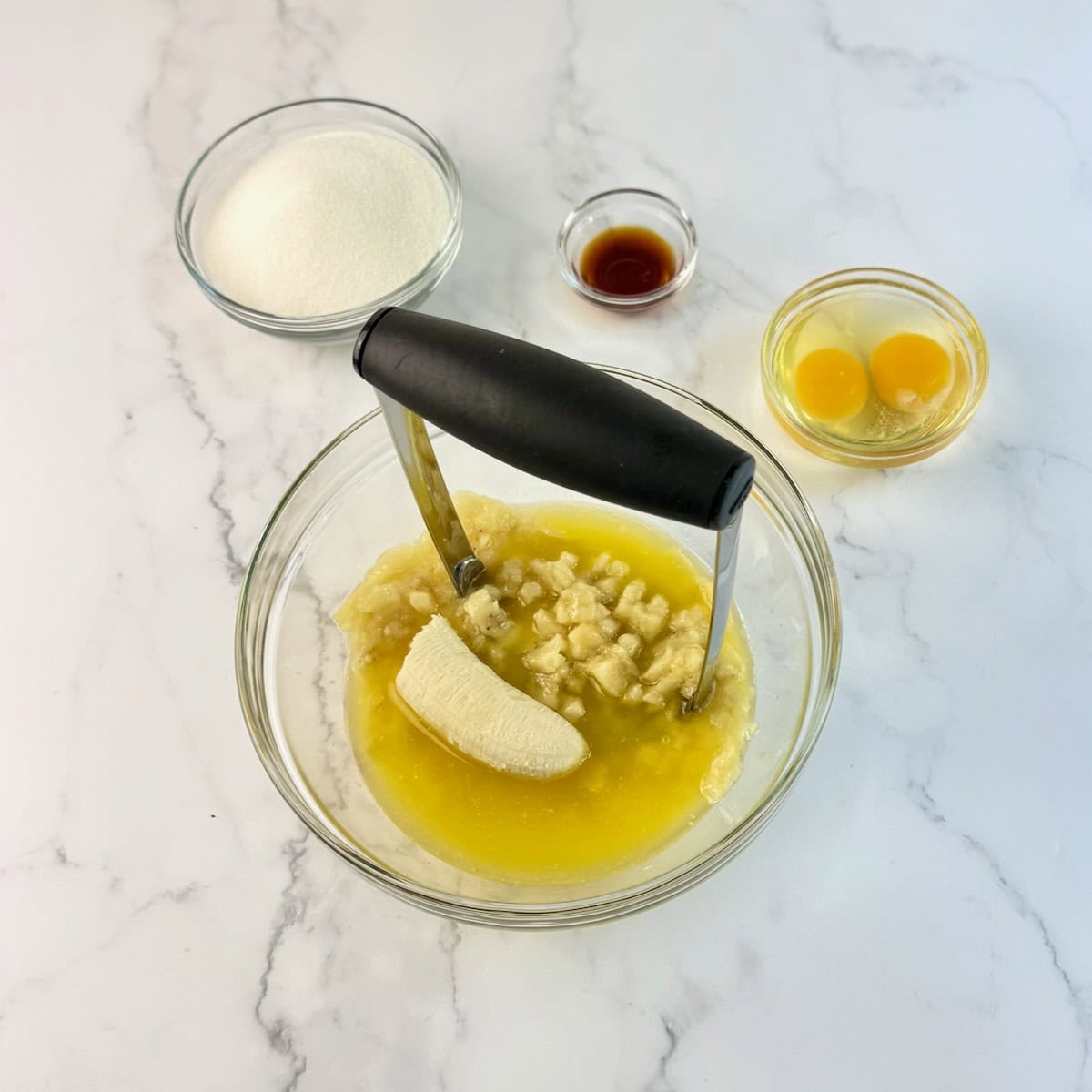Smashing bananas into a sugar and butter mixture with a potato masher.