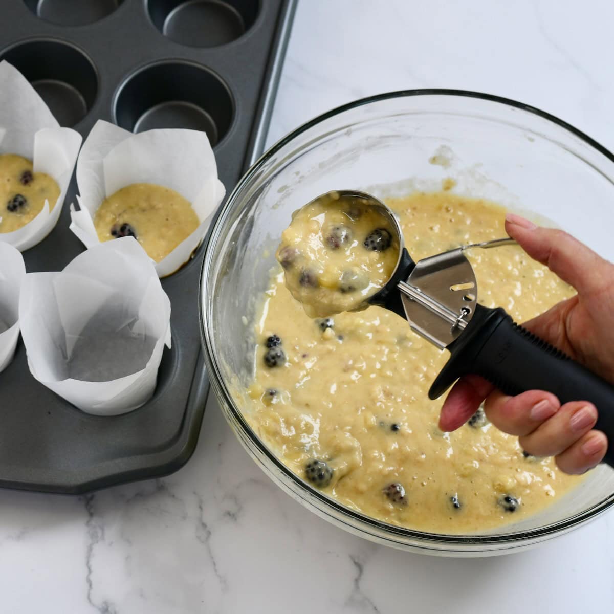 Using a cookie scoop to scoop muffin batter into the muffin tin.