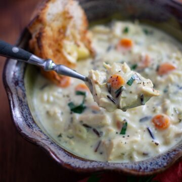 Spoonful of chicken wild rice soup hovering over a bowl of soup.