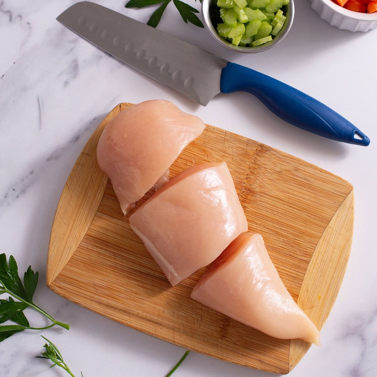 One raw chicken breast sliced into three pieces.