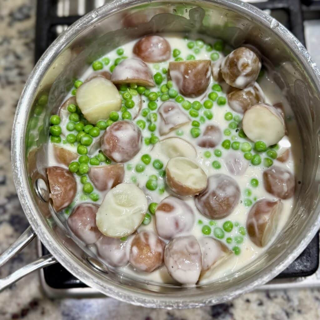Creamed potatoes and peas in a saucepan once the Alfredo sauce was added.