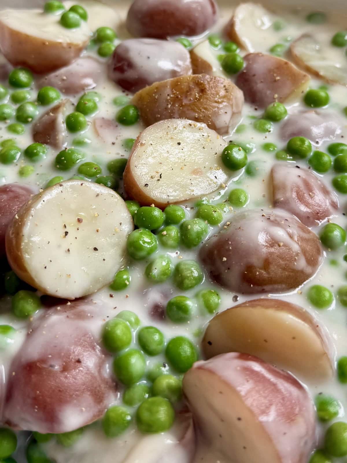 Close up of creamed potatoes and peas with cracked pepper on top.