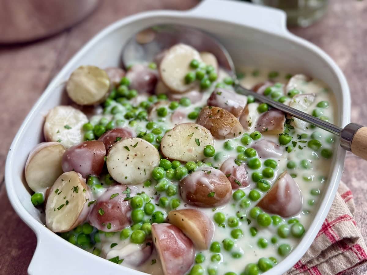 Finished creamed peas and potatoes in a baking dish with a serving spoon.