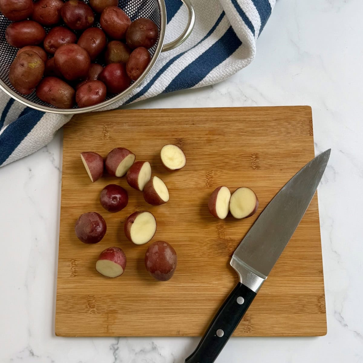 Slicing small potatoes in half on a wooden cutting board.