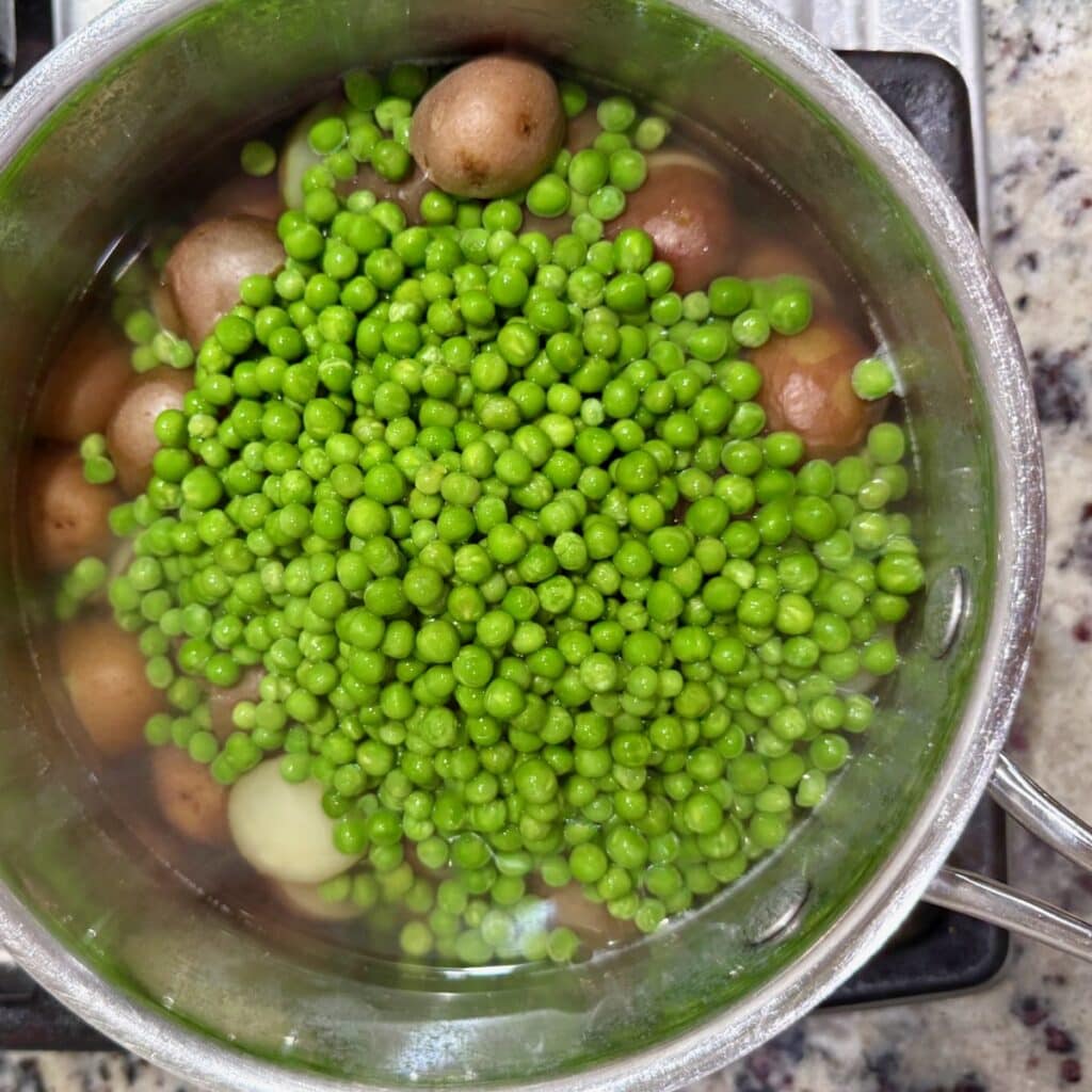 Peas added to the potatoes in a saucepan of water.