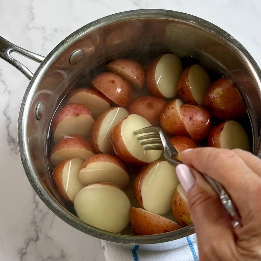 Fork testing a potato in a saucepan of boiled potatoes.