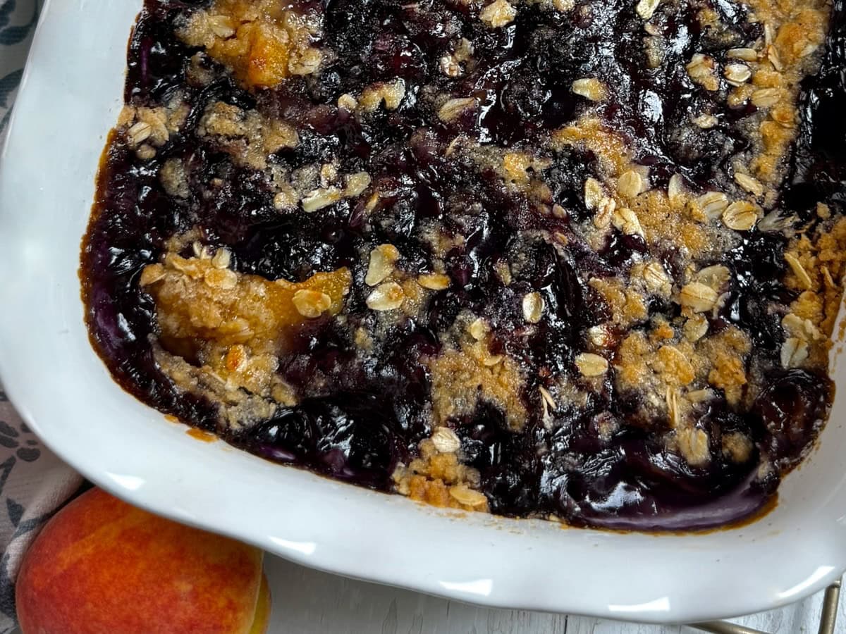 Close up of a corner of peach blueberry cobbler in a white baking dish.