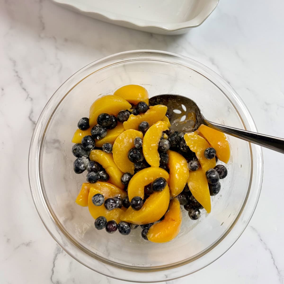 Mixing together sliced peaches with sugar in a mixing bowl.