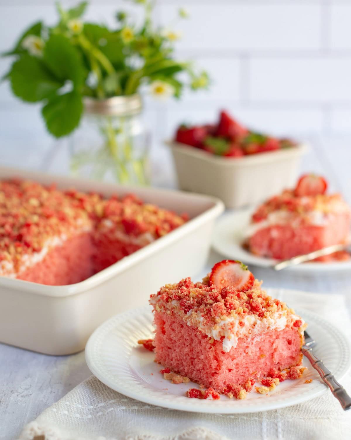 Two pieces of strawberry crunch cake on plate with more cake in a baking dish.