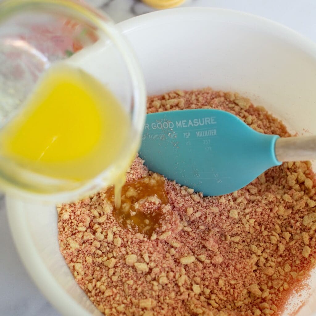 Pouring melted butter into the gelatin and Oreo mixture in a bowl.