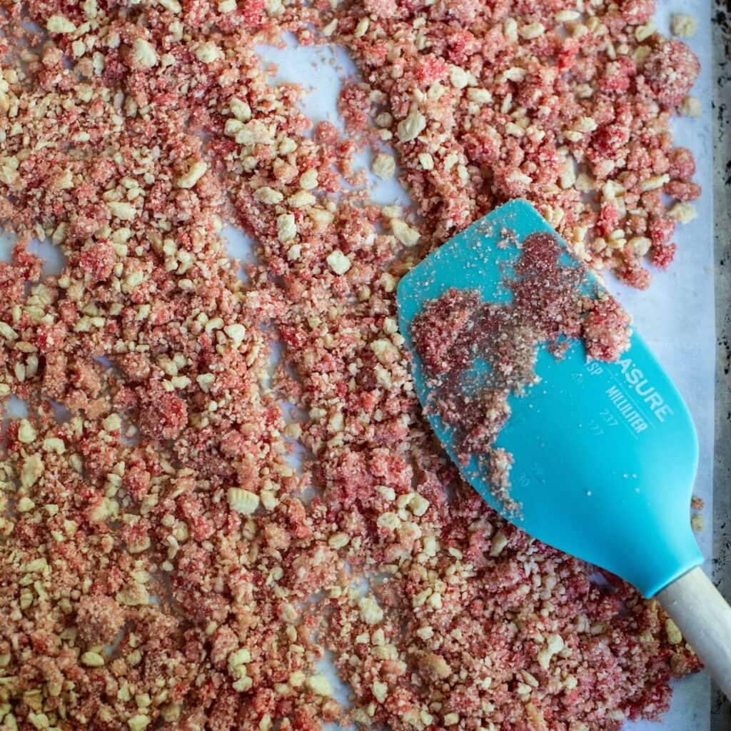 Rubber spatula spreading the strawberry crunch on a baking sheet.