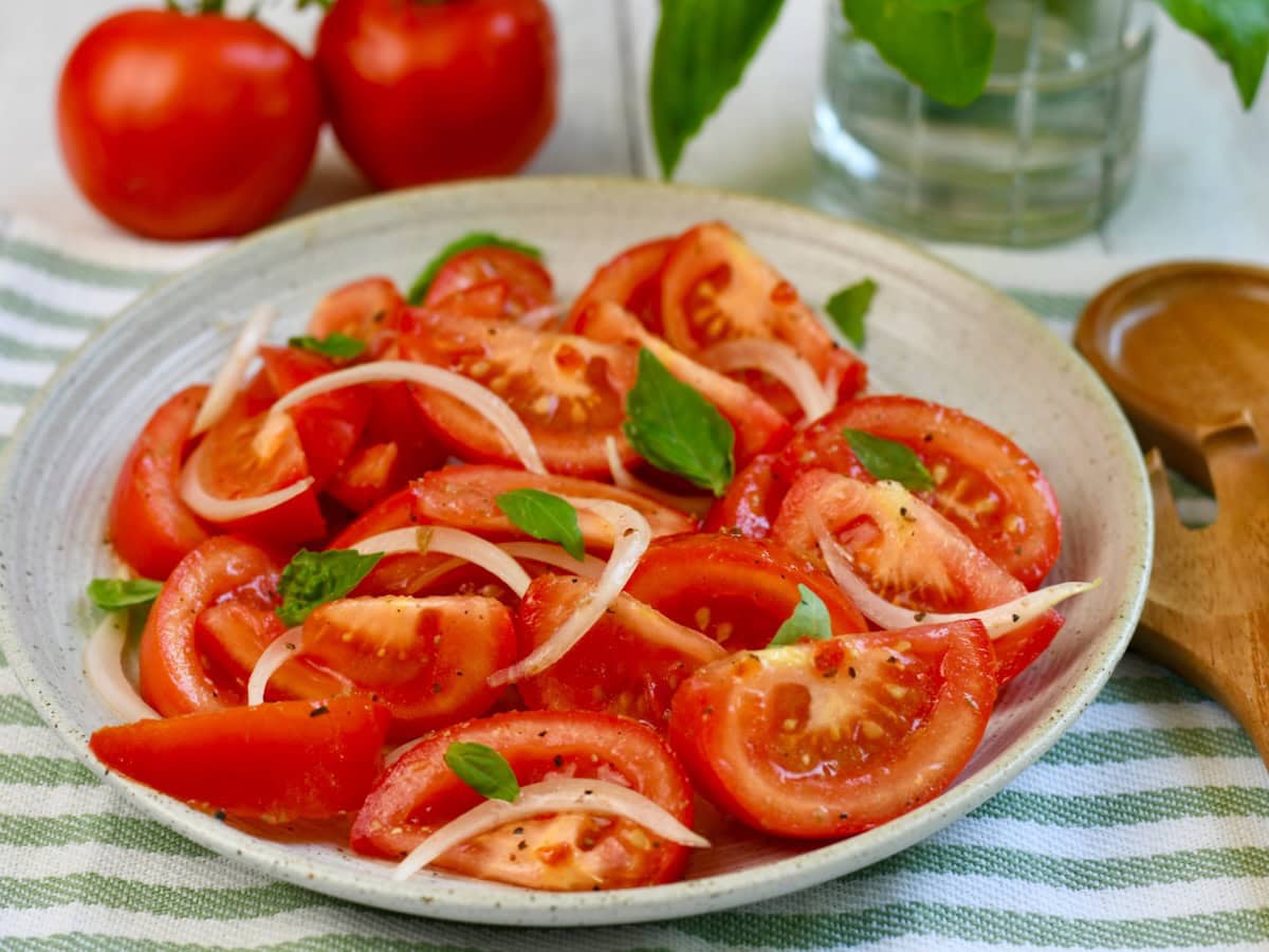 Side view of a tomato and onion salad in a bowl, garnished with basil.