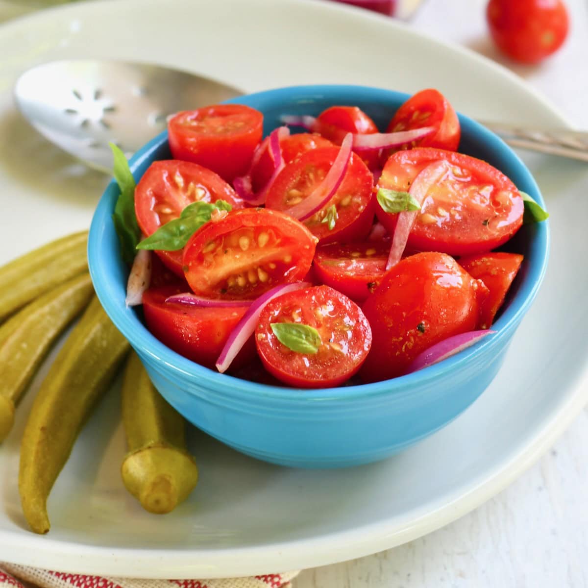 Tomato onion salad in a small blue bowl with basil leaves mixed in.