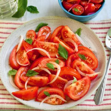 Tomato and onion salad in a large bowl with basil leaves.