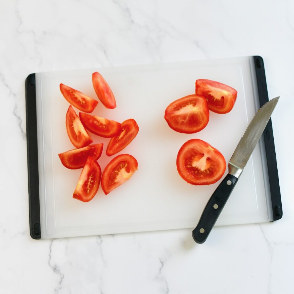 Sliced tomatoes into quarters on a cutting board.