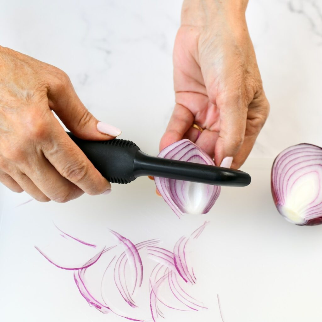 Using a potato peeler to slice thin slices of an onion.