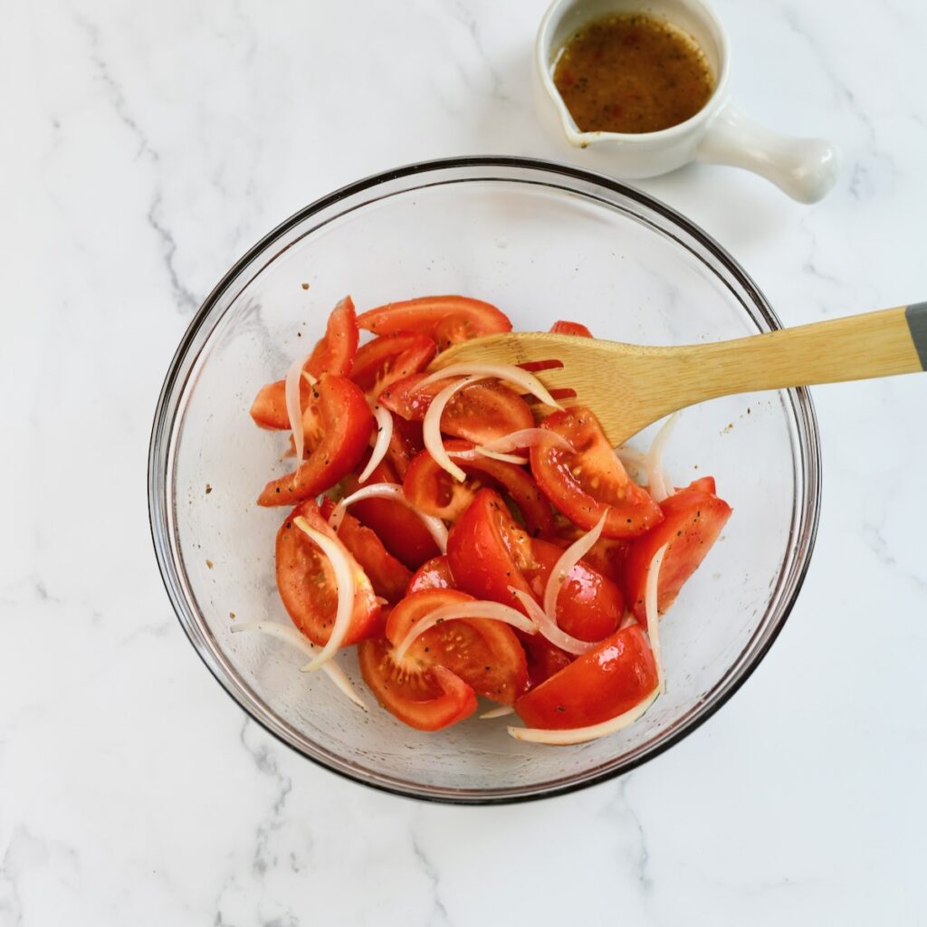 Sliced tomatoes and onions mixed with dressing in a bowl.