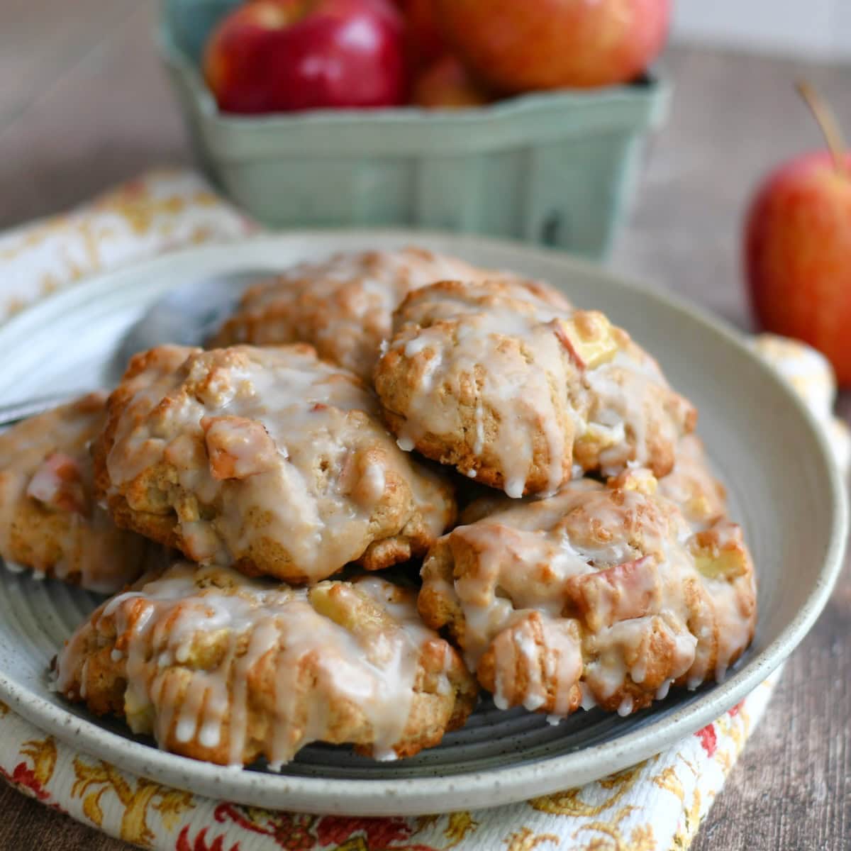 Baked apple fritters piled on a plate with fresh apples in the background.