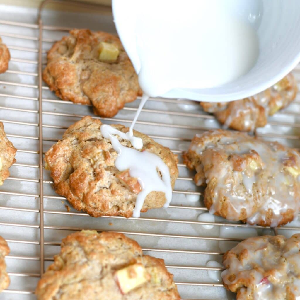 Drizzling icing on top of baked apple fritters.