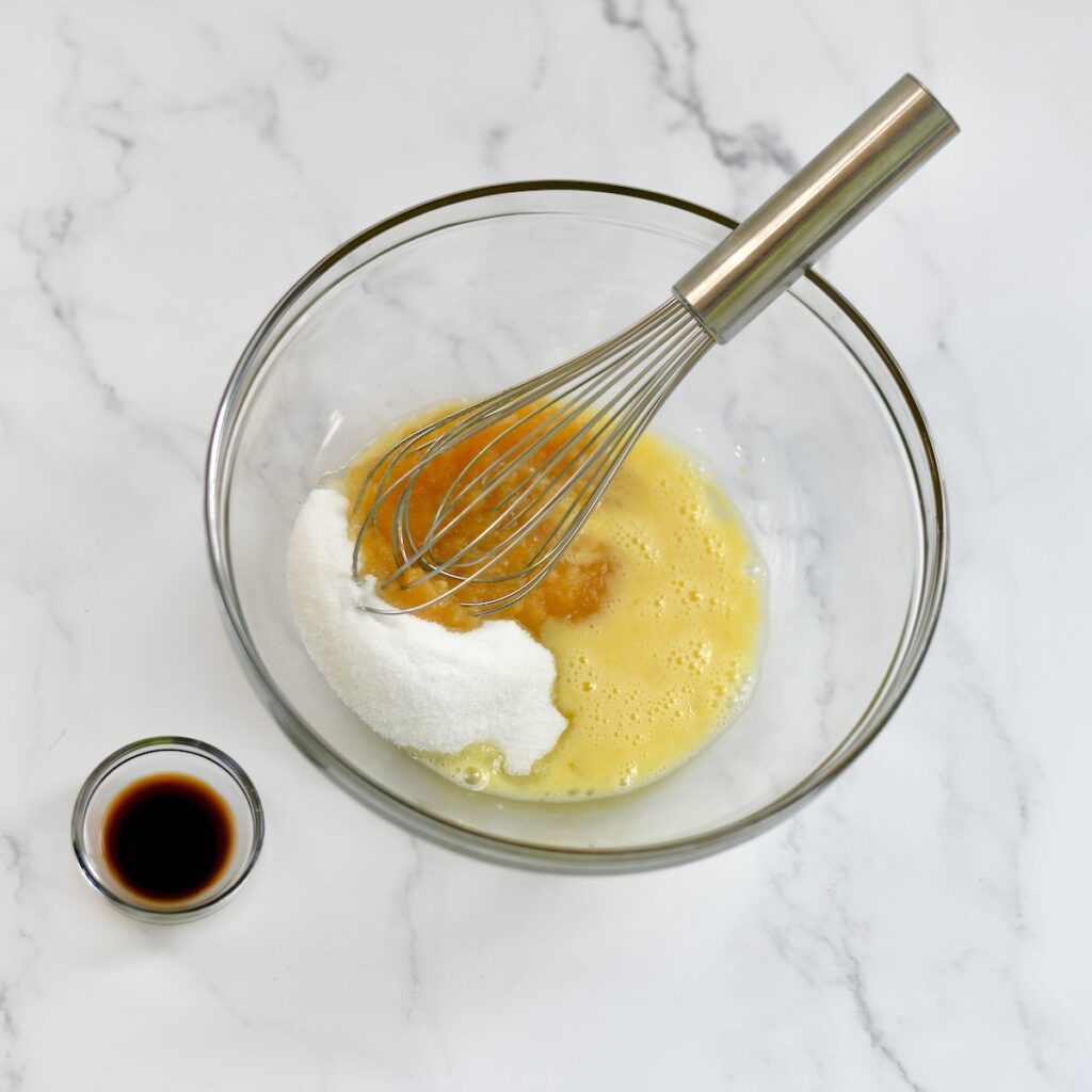 Whisking together apple sauce, sugar and eggs in a mixing bowl.