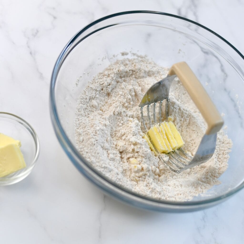 Using a pastry cutter to press butter into flour in a bowl.