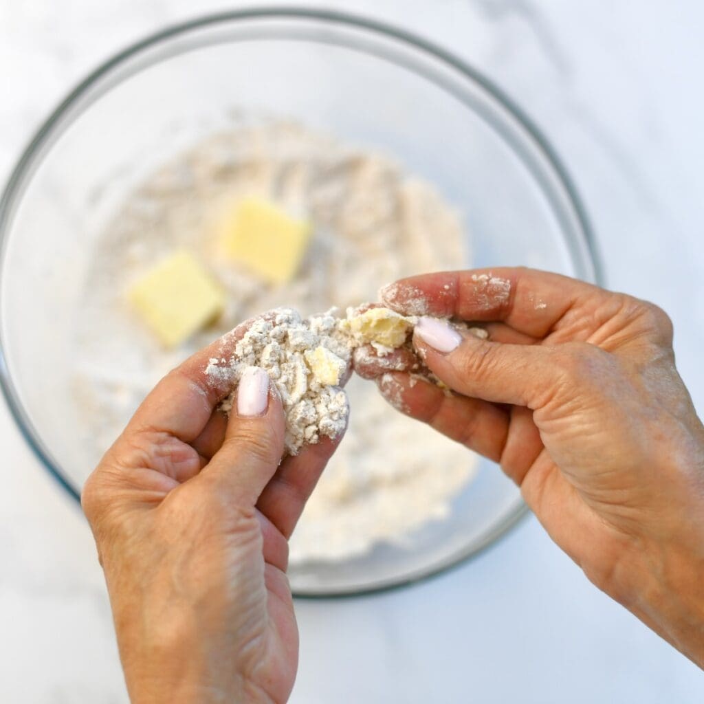 Hand holding flour with pieces of butter in it.