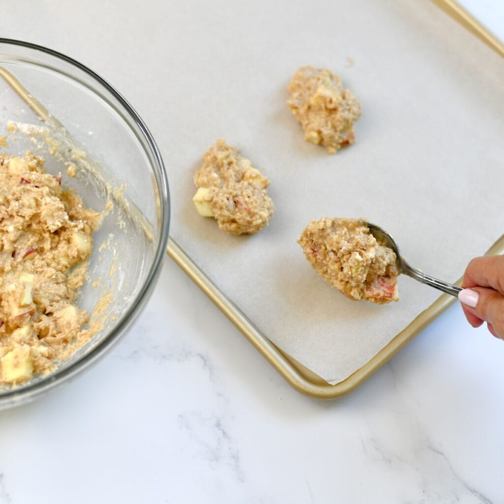 Spooning apple fritter dough onto a prepared sheet pan.
