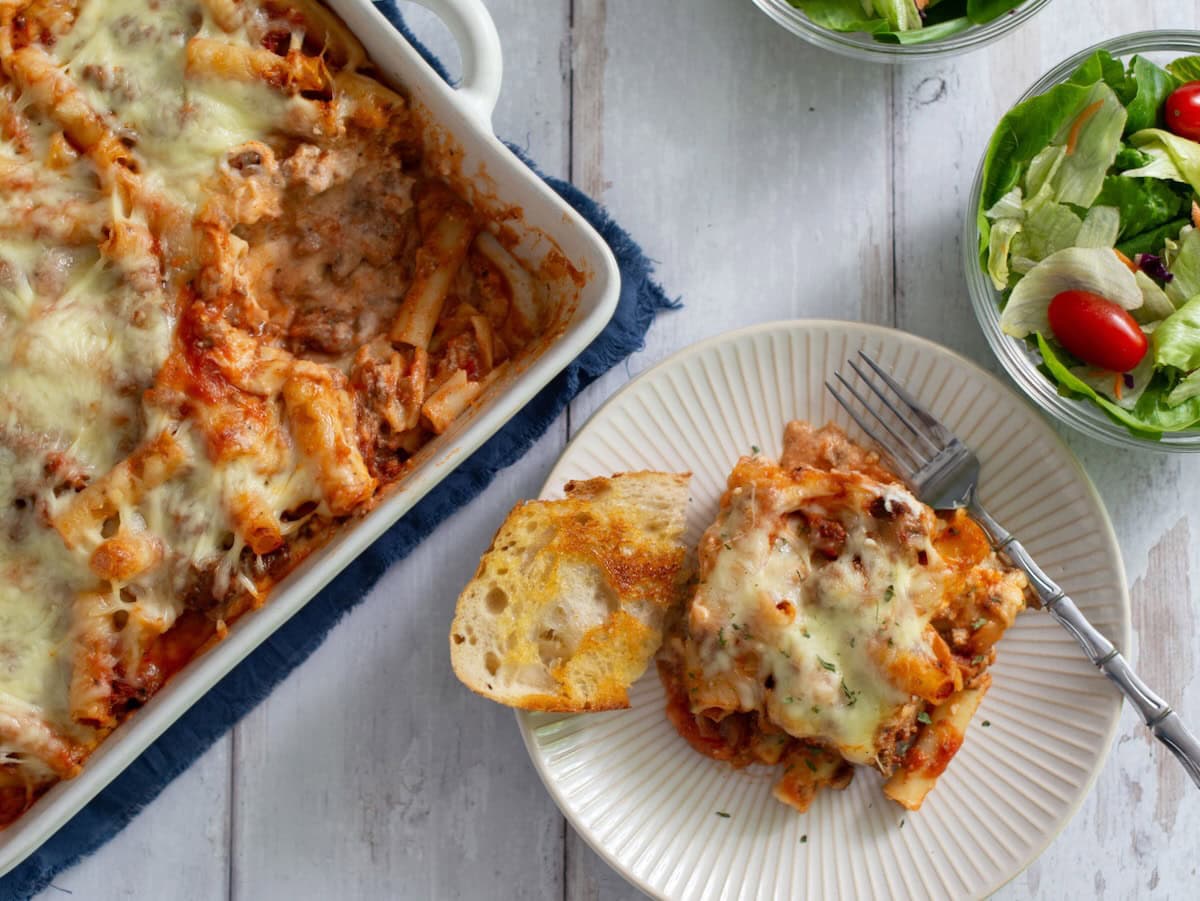 Portion of baked ziti on a plate next to a baking dish of baked ziti.
