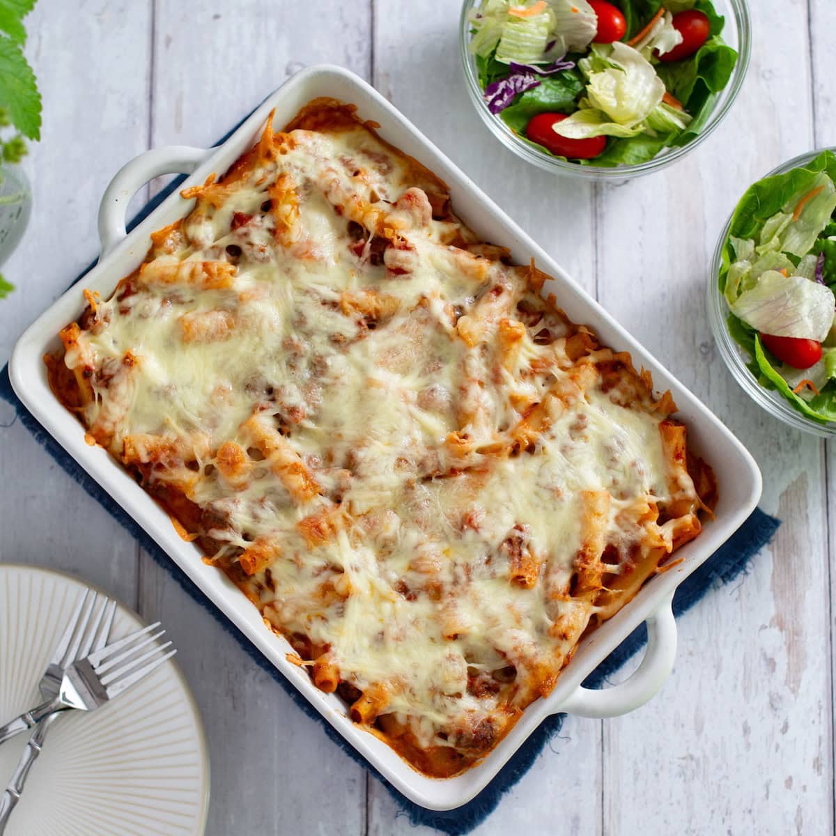 Overhead shot of easy baked ziti in a baking dish next to two small bowls of salad.