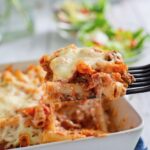 Portion of baked ziti on a spatula hovering over the baking dish of baked ziti.