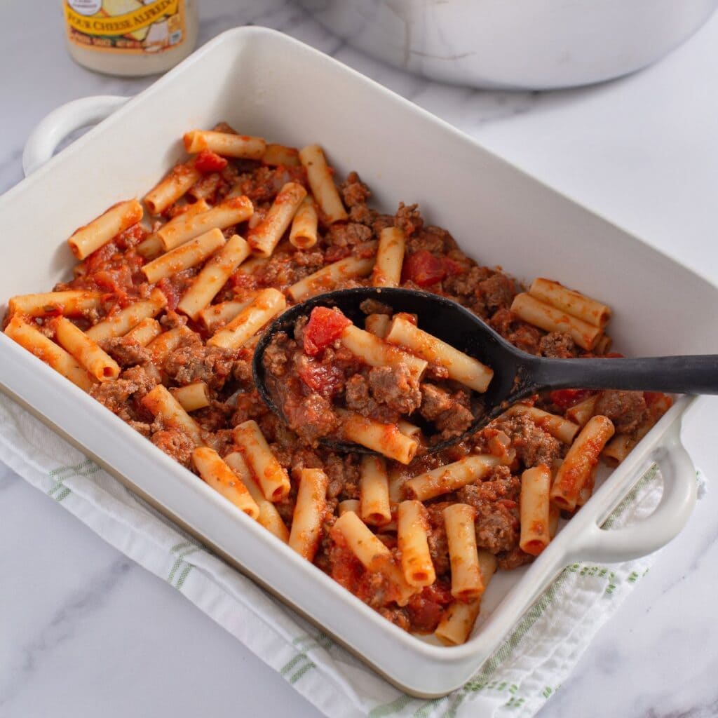 Pasta with meat sauce in the bottom of a baking dish.