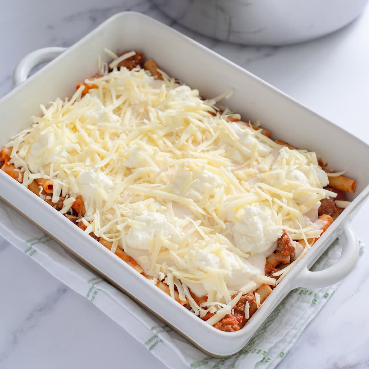 Shredded mozzarella placed on top of the layer of alfredo sauce in a baking dish.