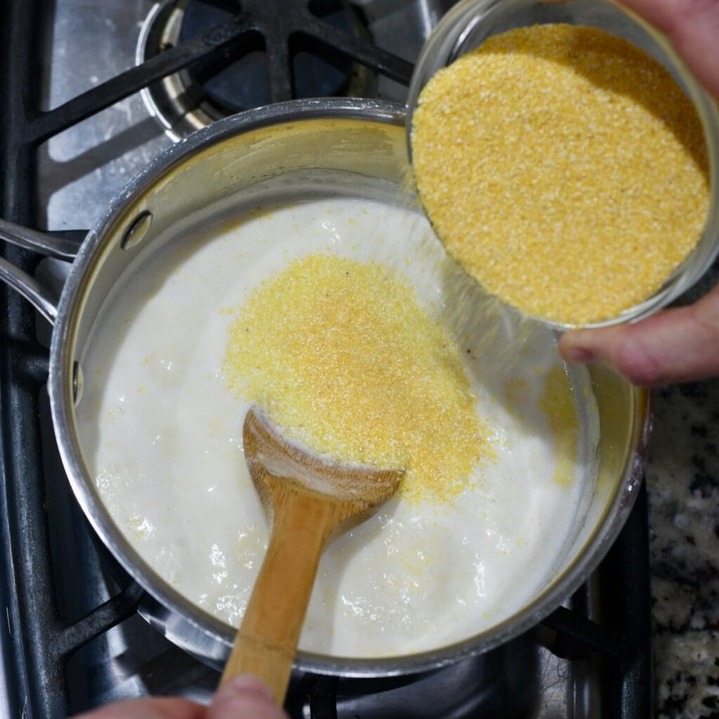 Pouring grits into the warm milk and broth mixture.
