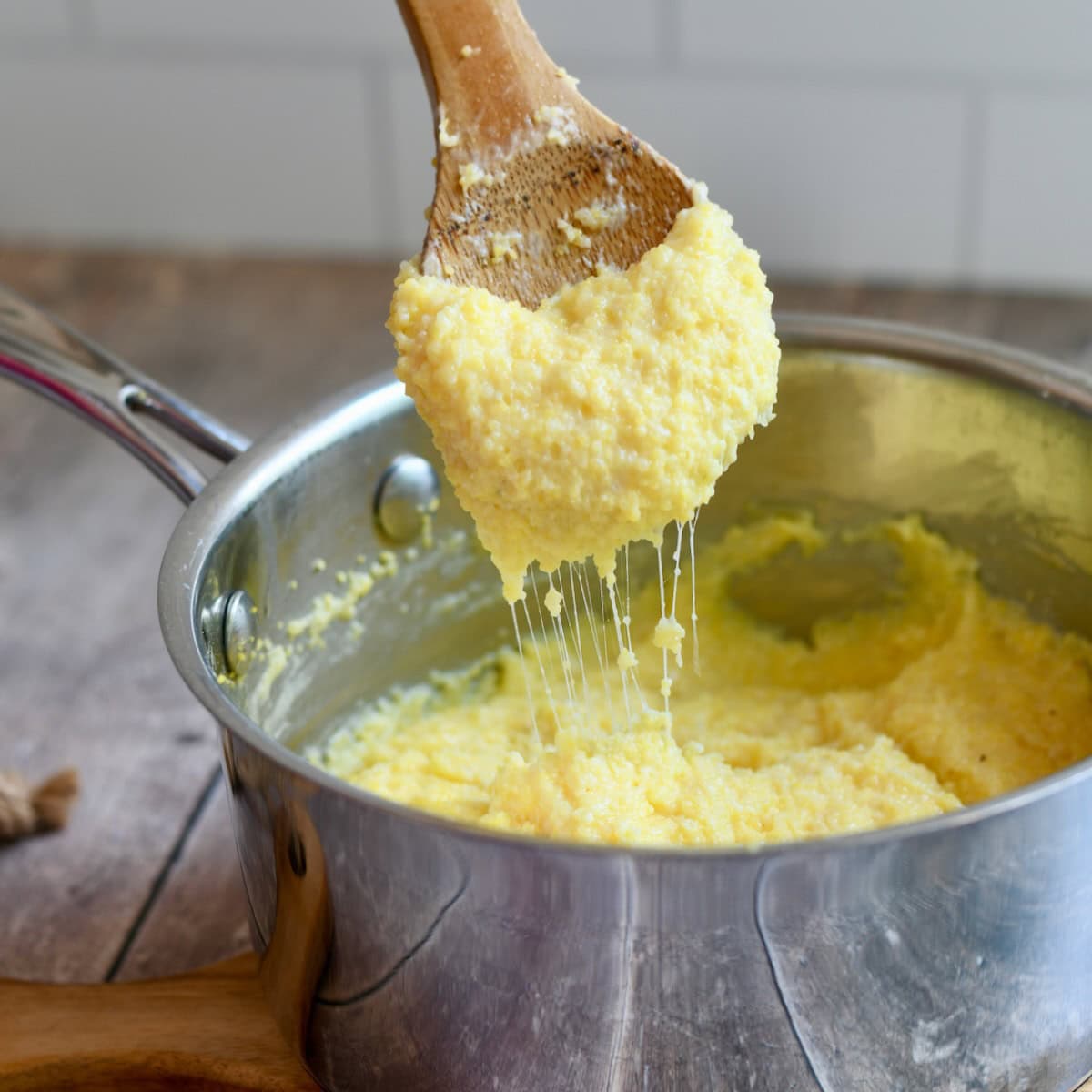Wooden spoon scooping up some gouda grits from a saucepan.