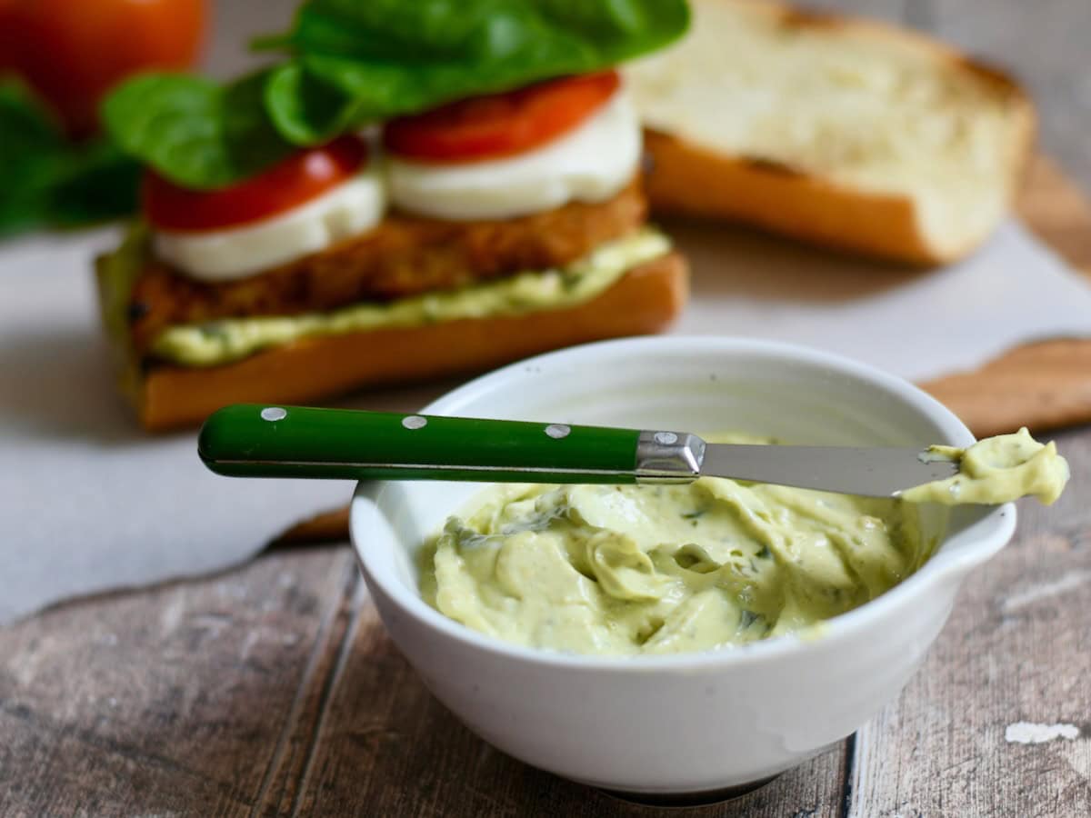 Side view of pesto mayo in a bowl with a spreading knife on top.