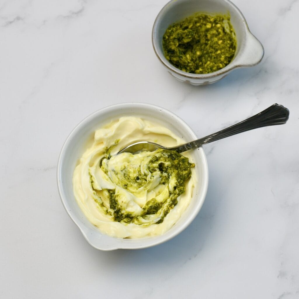 Mayo in a small bowl with pesto being stirred in.