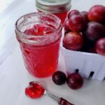 Muscadine jelly in a jar next to a pile of muscadine grapes.