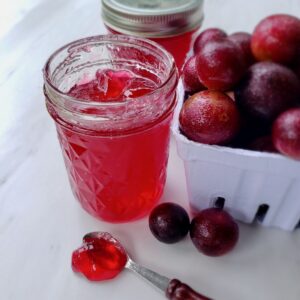 Muscadine jelly in a jar next to a pile of muscadine grapes.
