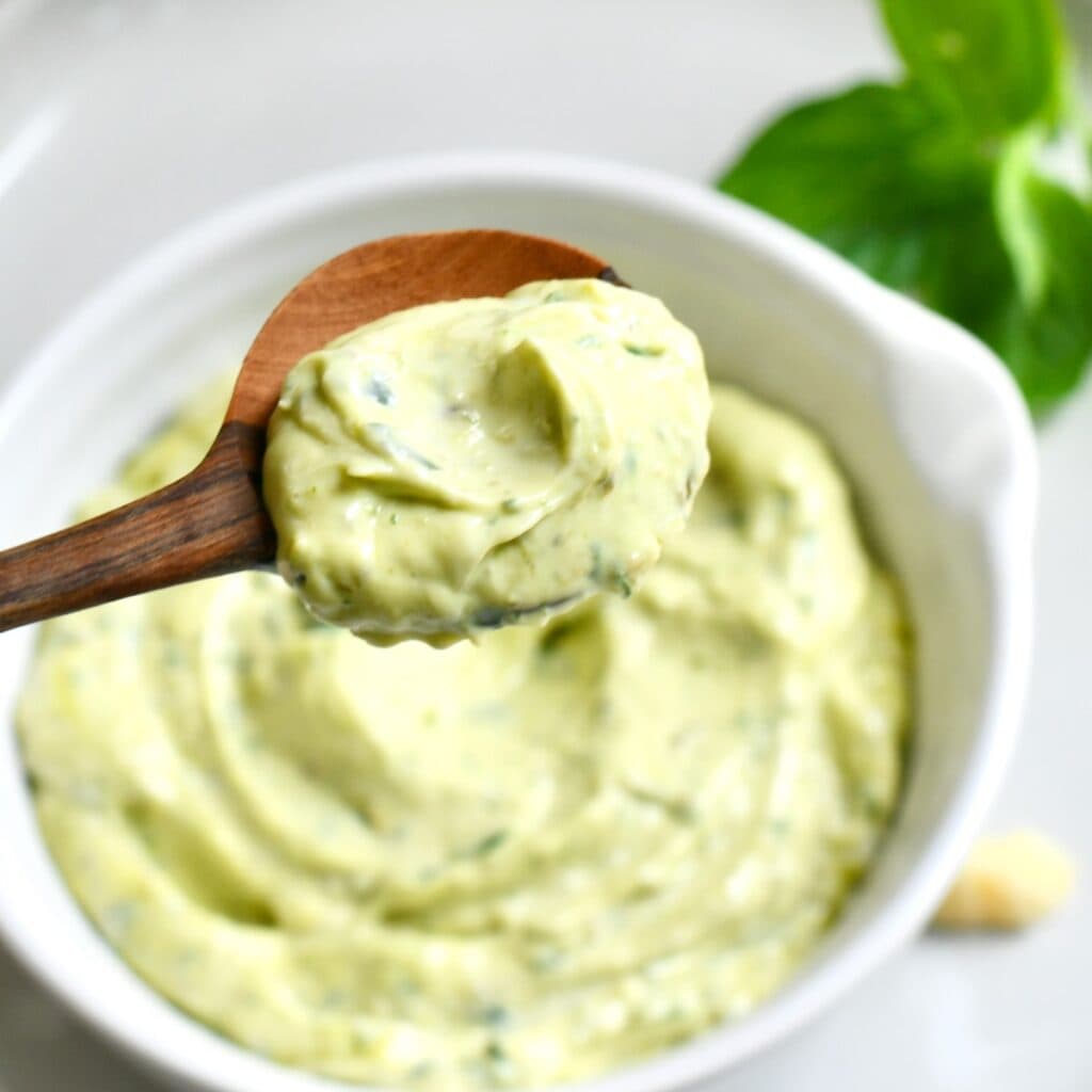 Spoon of pesto mayo hovering over a bowl of it.