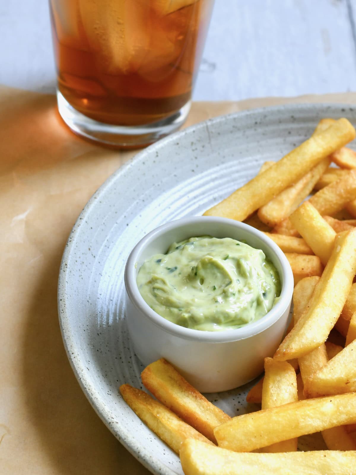Ramekin of pesto mayonnaise on a plate next to crispy french fries.