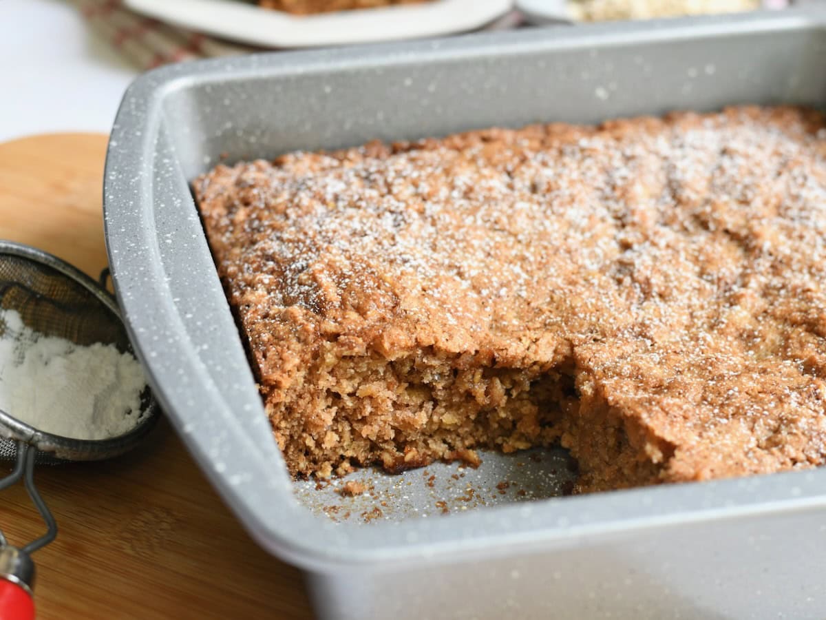 Side view of an apple oatmeal cake in a baking pan with one slice missing.