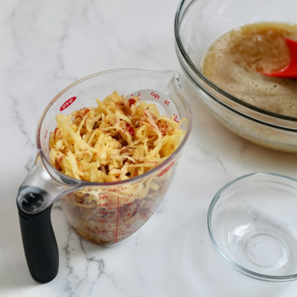 Two cups of shredded apples in a measuring cup.