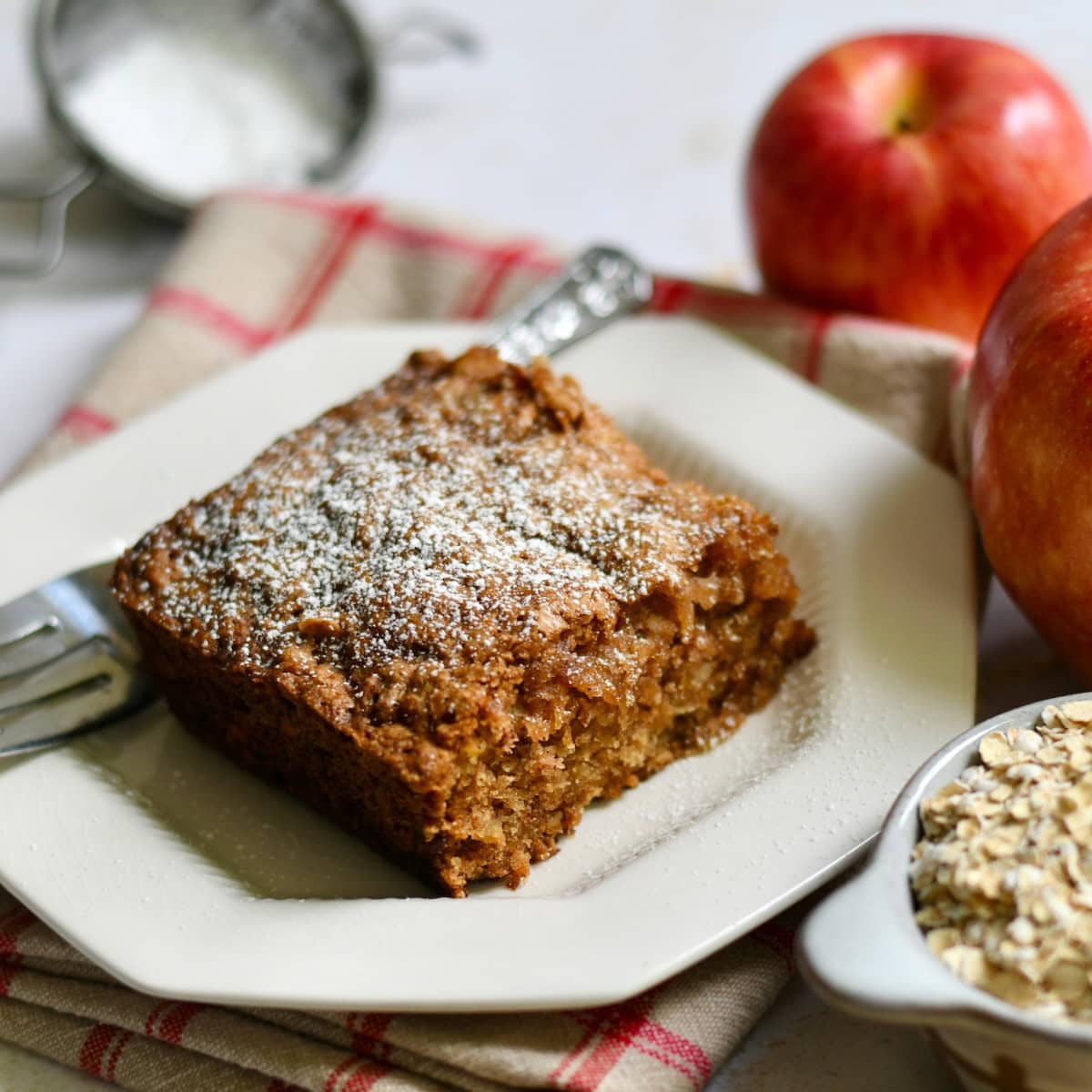 Apple oatmeal cake on a plate next to fresh apples.