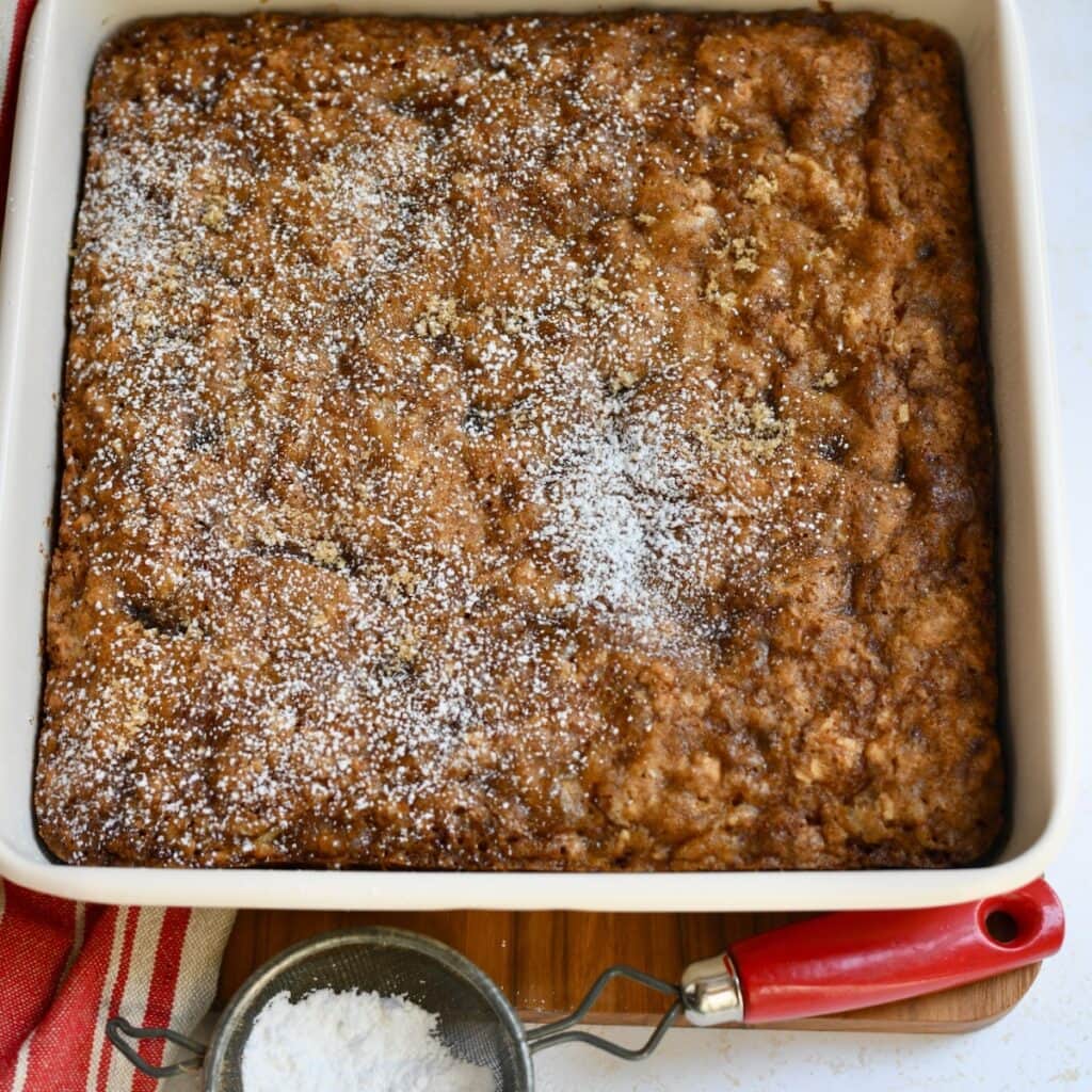 Sprinkling the powdered sugar over the top of the baked apple oatmeal cake.